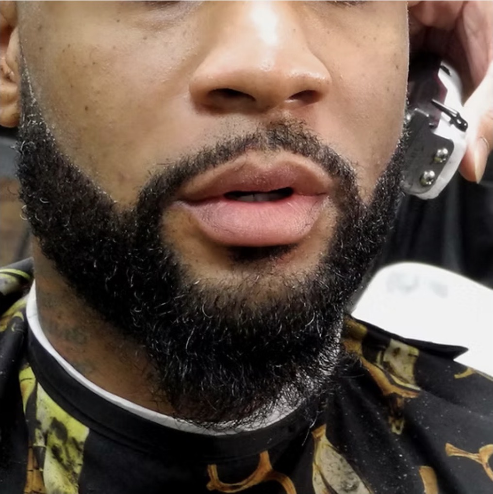 Close-up of a sharply shaped and lined beard being trimmed with clippers