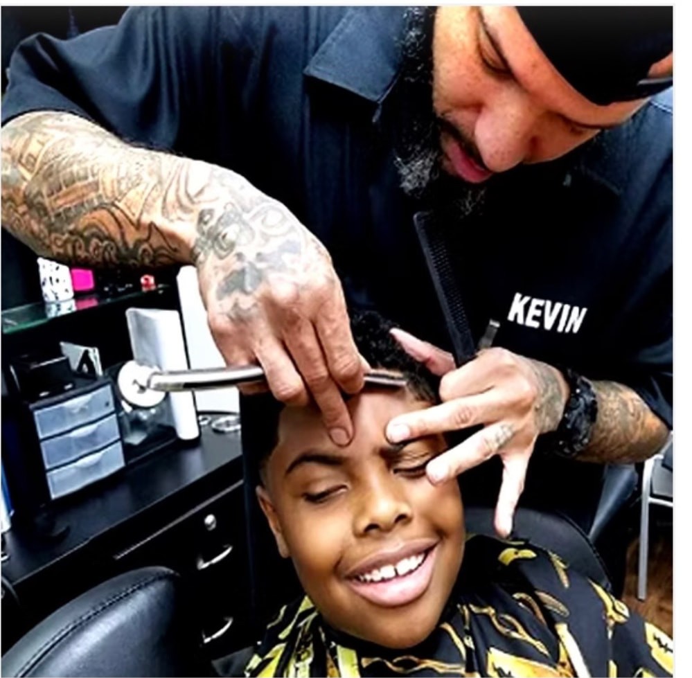 Kev razor-lining a smiling teen client's hairline in the barbershop
